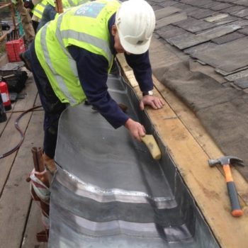 A photo of a man in high-vis and a hard hat cleaning lead on a historic roof